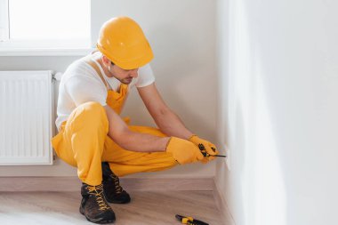 Handyman in yellow uniform works with electricity and installing new socket. House renovation conception.