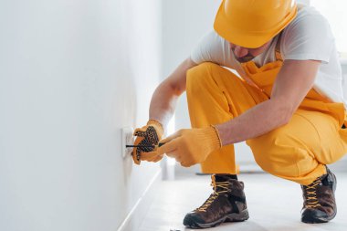Handyman in yellow uniform works with electricity and installing new socket. House renovation conception.