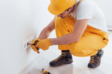 Handyman in yellow uniform works with electricity and installing new socket. House renovation conception.
