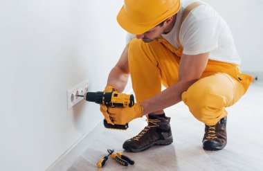Handyman in yellow uniform works with electricity and installing new socket by using automatic screwdriver. House renovation conception.