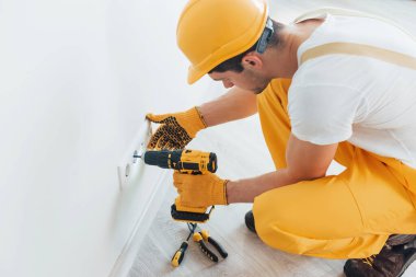 Handyman in yellow uniform works with electricity and installing new socket by using automatic screwdriver. House renovation conception.