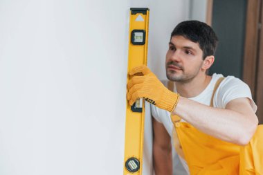 Handyman in yellow uniform checks levels of wall. House renovation conception.