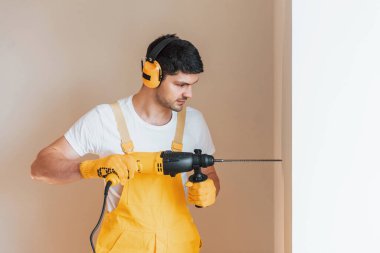 Handyman in yellow uniform works indoors by using hammer drill. House renovation conception.