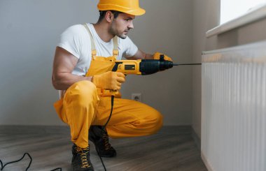 Handyman in yellow uniform works with drill indoors. House renovation conception.