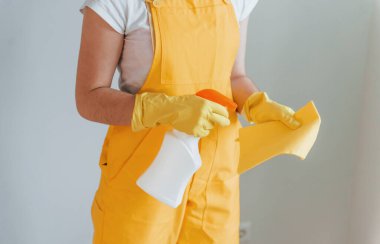 Housewife in yellow uniform preparing for polishing windows indoors. House renovation conception.