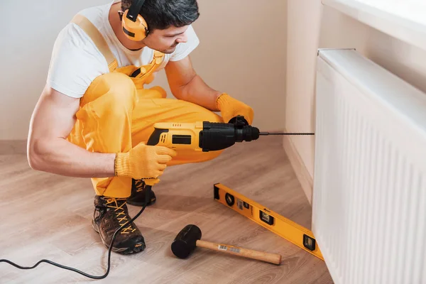 Handyman in yellow uniform works indoors by using hammer drill. House renovation conception.