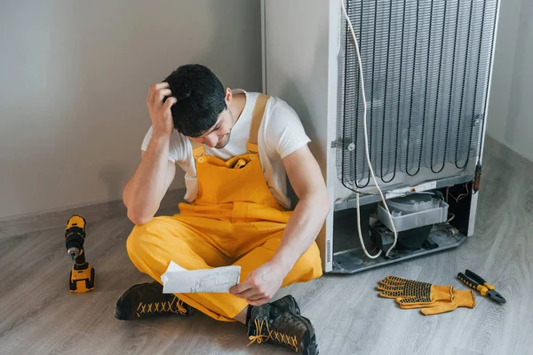 Confused Handyman Yellow Uniform Reading Manual Fridge Indoors House Renovation — Zdjęcie stockowe