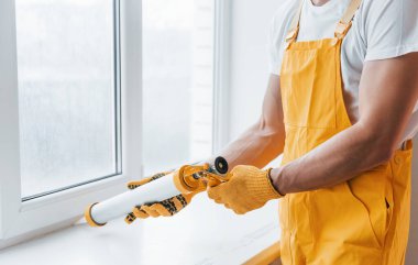 Sarı üniformalı tamirci içeride pencere için yapıştırıcı kullanıyor. Ev yenileme konsepti.