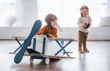 Retro pilot üniformalı iki küçük çocuk içeride oyuncak uçakla eğleniyor..