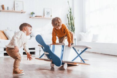 Two little boys in retro pilot uniform having fun with toy plane indoors.