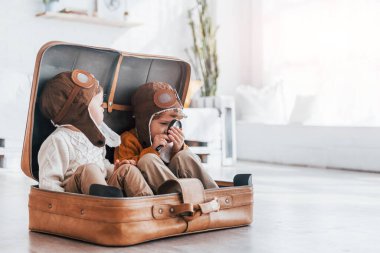 İki küçük çocuk eğleniyor ve gündüz vakti bavulun içinde oturuyor..