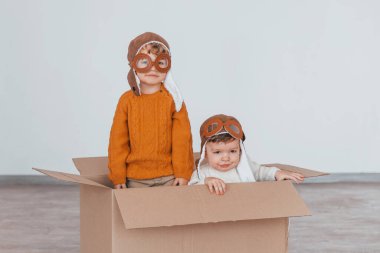 Retro pilot kostümlü iki küçük çocuk eğleniyor ve gündüz vakti kağıt kutunun içinde oturuyor..