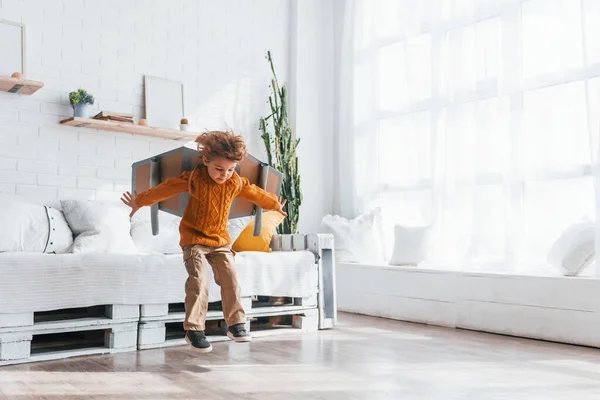 Little boy in retro pilot uniform running with toy plane indoors.