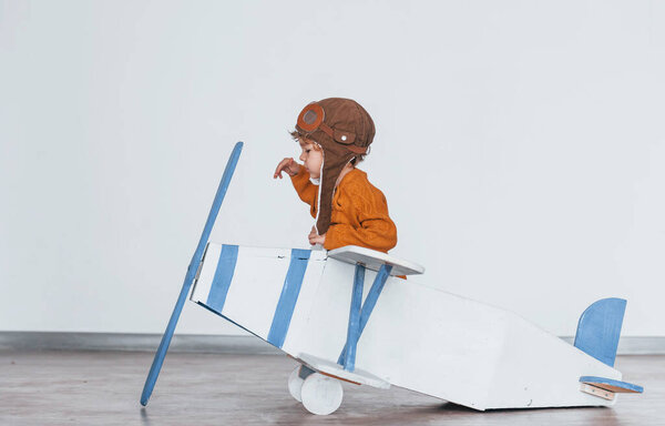 Мальчик в форме ретро-пилота веселится с игрушечным самолетом в помещении.
