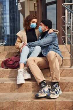Karantina zamanında iş binasının yakınında birbirini kucaklayan koruyucu maskeli bir çift. Koronavirüs kavramı.