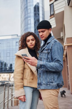 Telefonla. Sıcak giysiler içinde neşeli bir çift şehir dışında iş binasının yanında yürüyüş yapıyor..