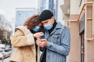 Karantina zamanında iş binasının yakınında antiseptik kullanan koruyucu maskeli bir çift. Koronavirüs kavramı.