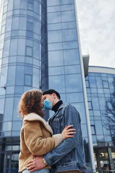 Karantina zamanında iş binasının yakınında koruyucu maskeli bir çift birbirini öpüyor. Koronavirüs kavramı.