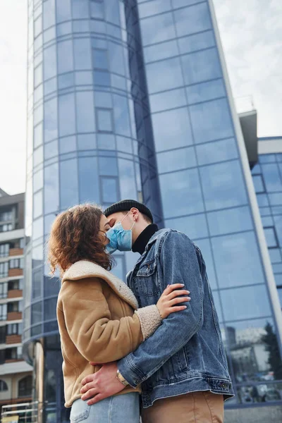 Karantina zamanında iş binasının yakınında koruyucu maskeli bir çift birbirini öpüyor. Koronavirüs kavramı.
