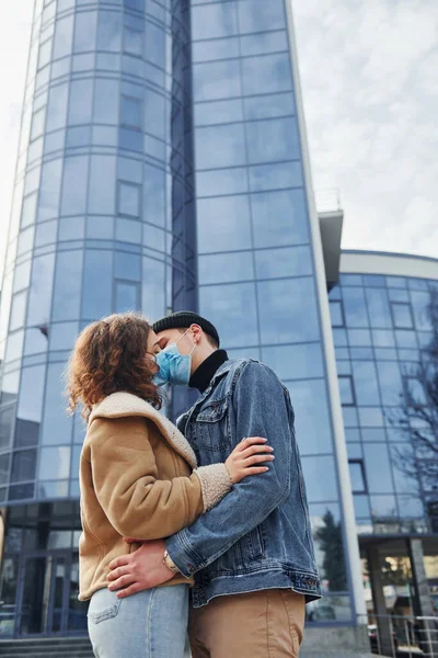Karantina zamanında iş binasının yakınında koruyucu maskeli bir çift birbirini öpüyor. Koronavirüs kavramı.