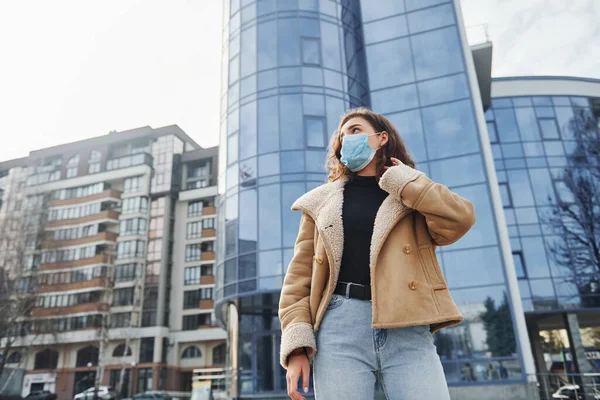 Karantina zamanında iş yerinin yakınında duran koruyucu maskeli kıvırcık saçlı genç kızın portresi. Koronavirüs kavramı.