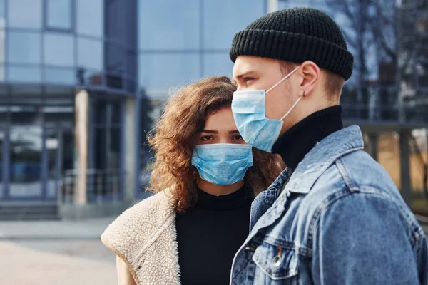 Koruyucu maskeli bir çift, karantina zamanında iş binasının yakınında şehir dışında yürüyüş yapıyor. Koronavirüs kavramı.