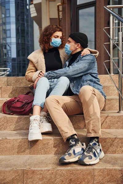 Karantina zamanında iş binasının yakınında birbirini kucaklayan koruyucu maskeli bir çift. Koronavirüs kavramı.