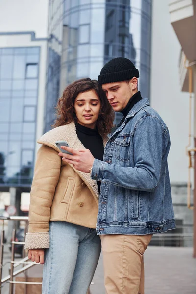 Telefonla. Sıcak giysiler içinde neşeli bir çift şehir dışında iş binasının yanında yürüyüş yapıyor..