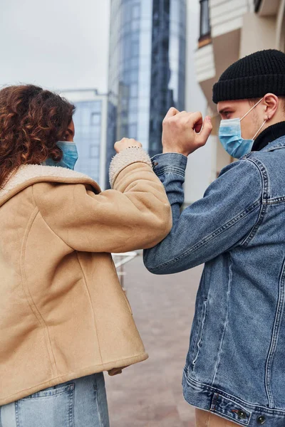 Couple in protective masks greeting each other in the city near business building at quarantine time. Conception of coronavirus.