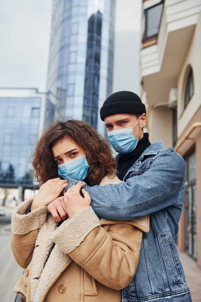Karantina zamanında iş binasının yakınında birbirini kucaklayan koruyucu maskeli bir çift. Koronavirüs kavramı.