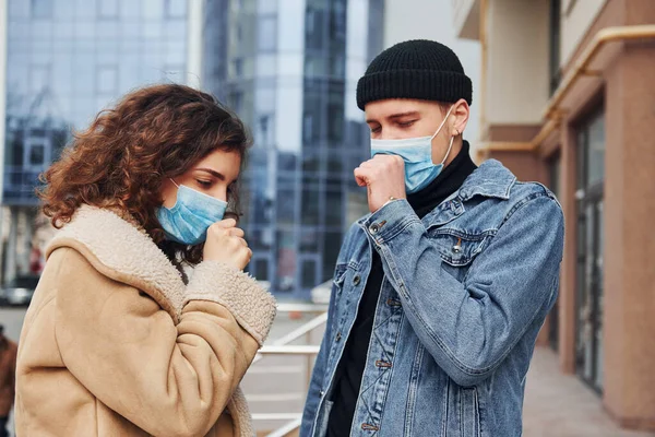 Koruyucu maskeli bir çift karantina zamanında iş binasının yakınında dışarıda öksürüyorlar. Koronavirüs kavramı.