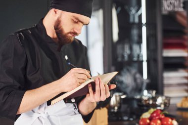 Professional young chef cook in uniform standing with notepad on the kitchen.