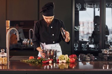 Ekipman kullanarak. Üniformalı profesyonel aşçı mutfakta sebzelerle çalışıyor..