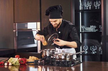 Ekipman kullanarak. Üniformalı profesyonel aşçı mutfakta sebzelerle çalışıyor..