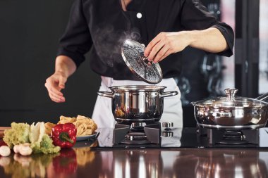 Ekipman kullanarak. Üniformalı profesyonel aşçı mutfakta sebzelerle çalışıyor..