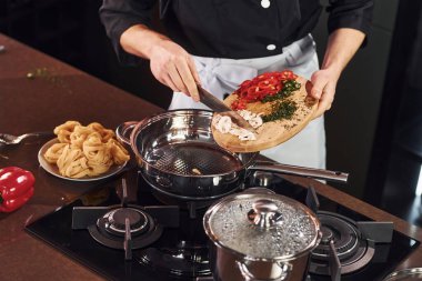 Ekipman kullanarak. Üniformalı profesyonel aşçı mutfakta sebzelerle çalışıyor..