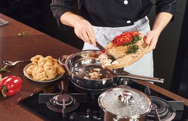 Ekipman kullanarak. Üniformalı profesyonel aşçı mutfakta sebzelerle çalışıyor..