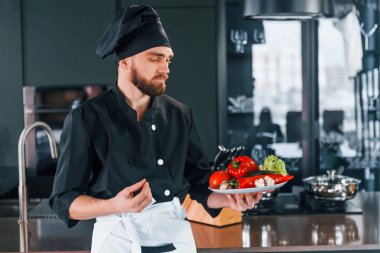 Üniformalı profesyonel aşçı mutfakta sebze tabağı tutuyor..