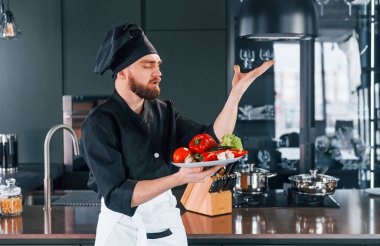 Üniformalı profesyonel aşçı mutfakta sebze tabağı tutuyor..