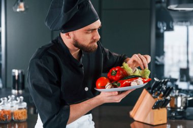 Üniformalı profesyonel aşçı mutfakta sebze tabağı tutuyor..