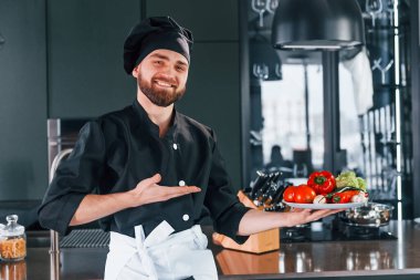 Üniformalı profesyonel aşçı mutfakta sebze tabağı tutuyor..