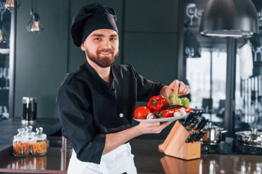 Üniformalı profesyonel aşçı mutfakta sebze tabağı tutuyor..