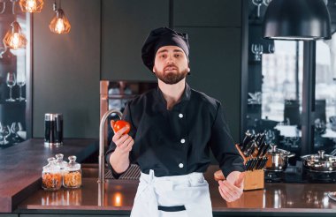 Profesyonel aşçı üniforması içinde masanın yanında duruyor ve mutfakta kameraya poz veriyor..