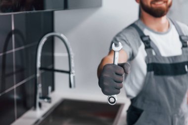 Gri üniformalı genç profesyonel tesisatçının mutfağın anahtarı elindeyken yakın plan görüntüsü..