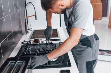 Young professional plumber in grey uniform working on the kitchen.