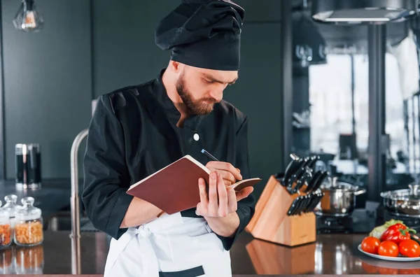 Professional young chef cook in uniform standing with notepad on the kitchen.