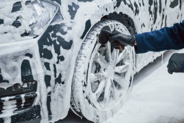 Üniformalı bir erkek işçi sabunla kaplanmış modern bir arabayı yıkıyor. Hizmet kavramı.