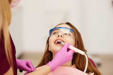 Koruyucu gözlüklü küçük kız klinikteki dişçiyi ziyaret ediyor. Stomatoloji kavramı.