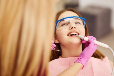 Koruyucu gözlüklü küçük kız klinikteki dişçiyi ziyaret ediyor. Stomatoloji kavramı.