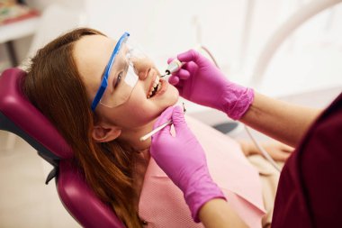 Koruyucu gözlüklü küçük kız klinikteki dişçiyi ziyaret ediyor. Stomatoloji kavramı.